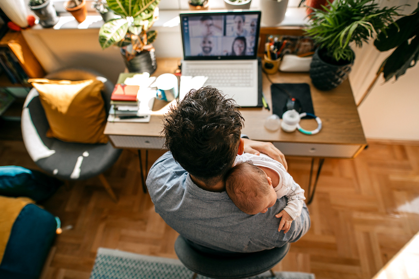 Photo of a man working from home, with his newborn baby as a company, having a video conference call