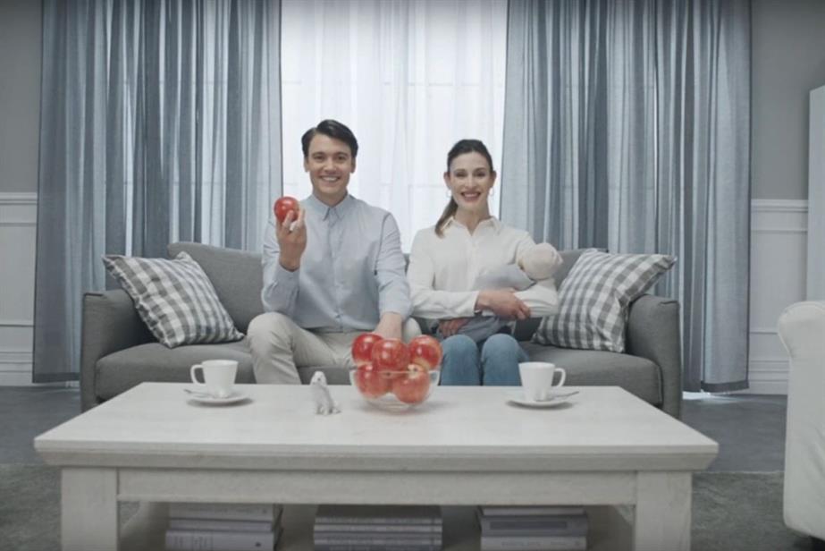 A couple sitting on a grey sofa posing as if in a catalogue